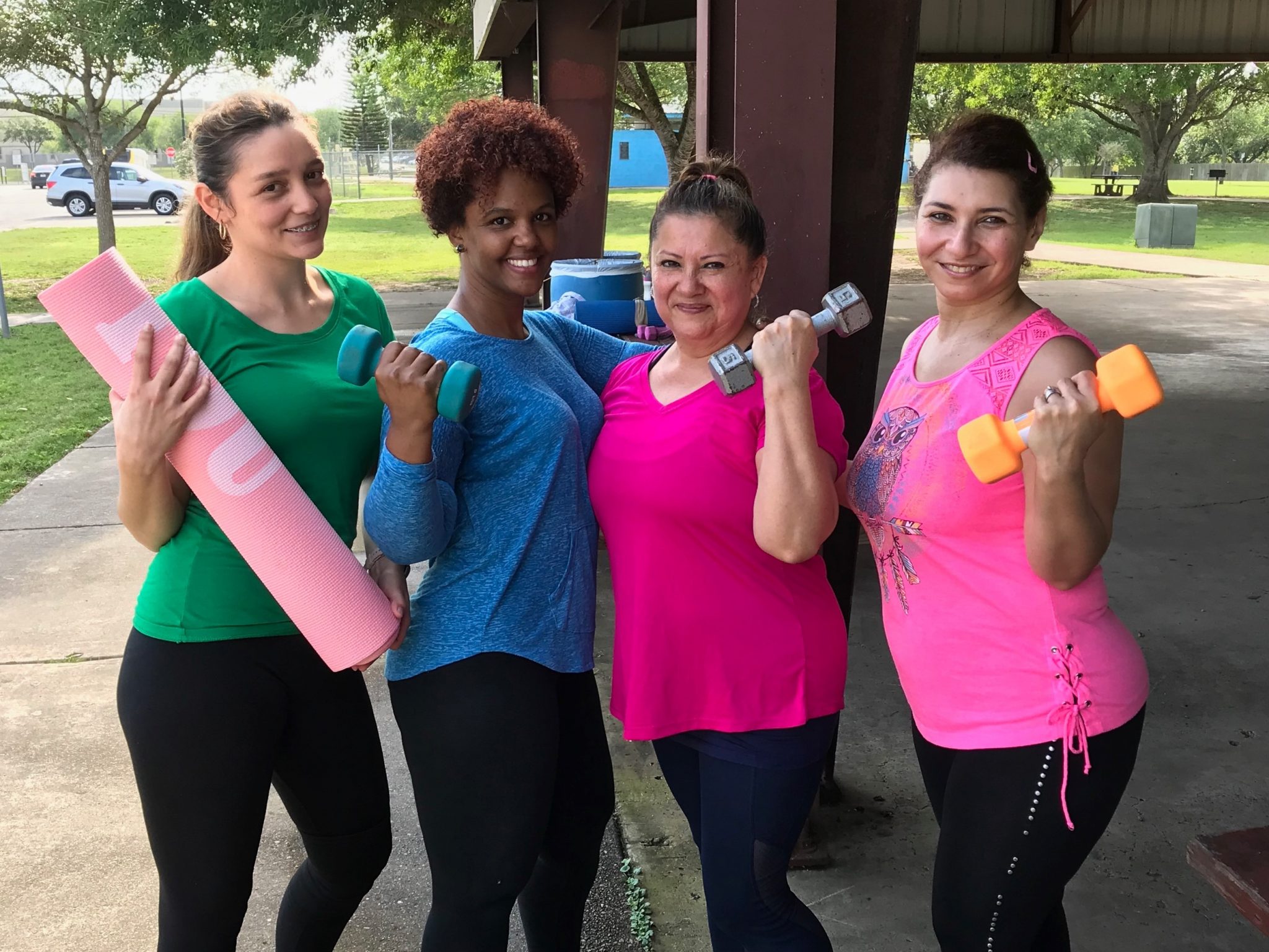 A group of women flexing and posing for a photo during an outdoor exercise class